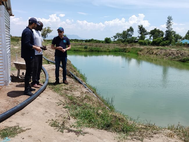 Three men standing beside a pond.
