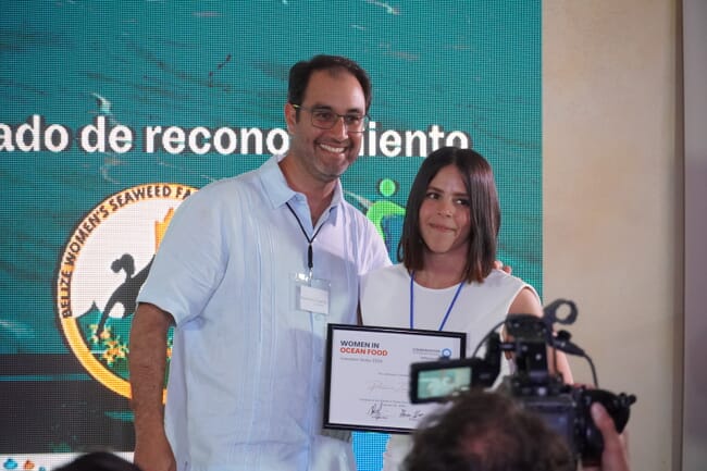 Two people holding a certificate on a stage.